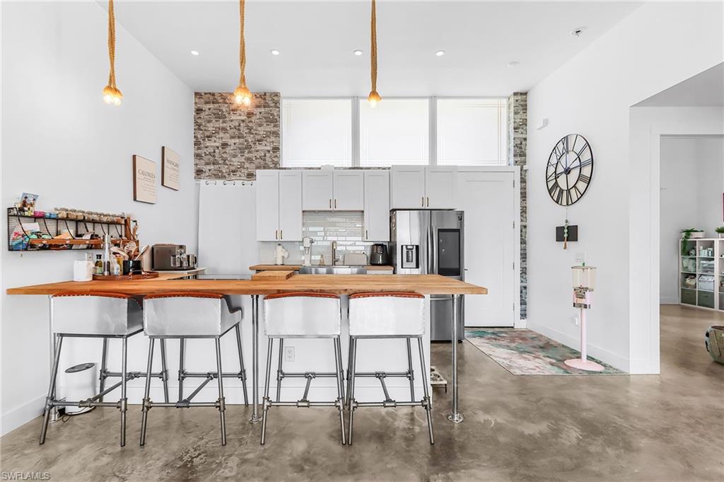 Kitchen featuring a peninsula, a breakfast bar area, stainless steel refrigerator with ice dispenser, finished concrete flooring, and white cabinets