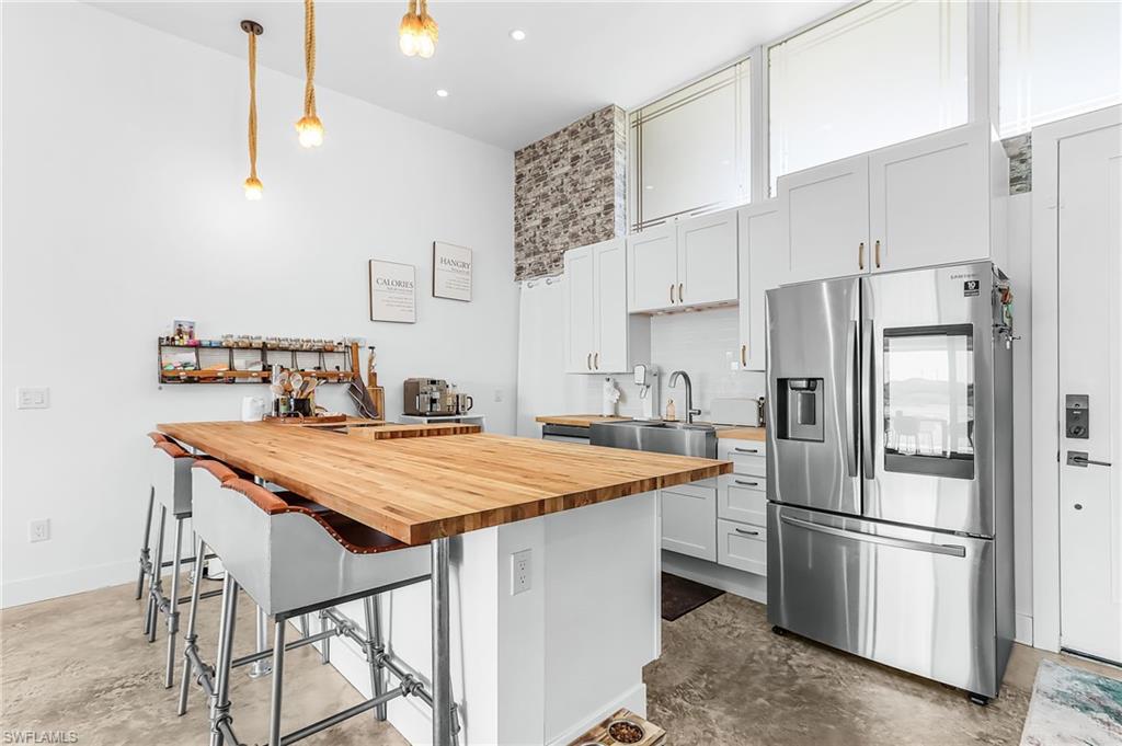 Kitchen with stainless steel fridge, unfinished concrete flooring, wooden counters, and pendant lighting