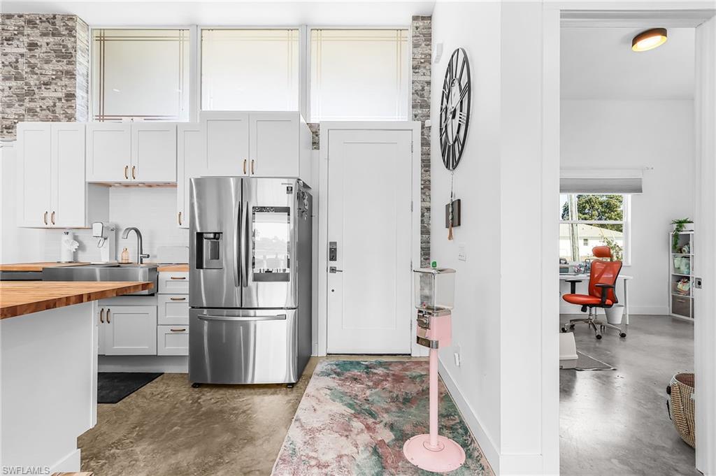 Kitchen featuring stainless steel fridge, white cabinetry, butcher block counters, concrete flooring, and an office area