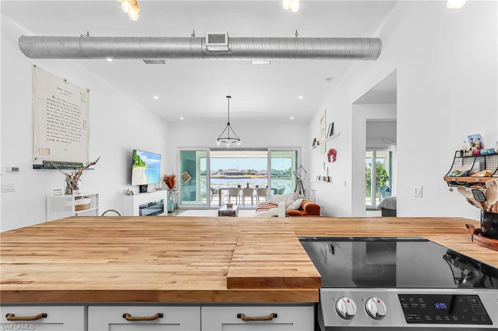 Kitchen with wood counters, stainless steel electric range oven, open floor plan, and hanging light fixtures