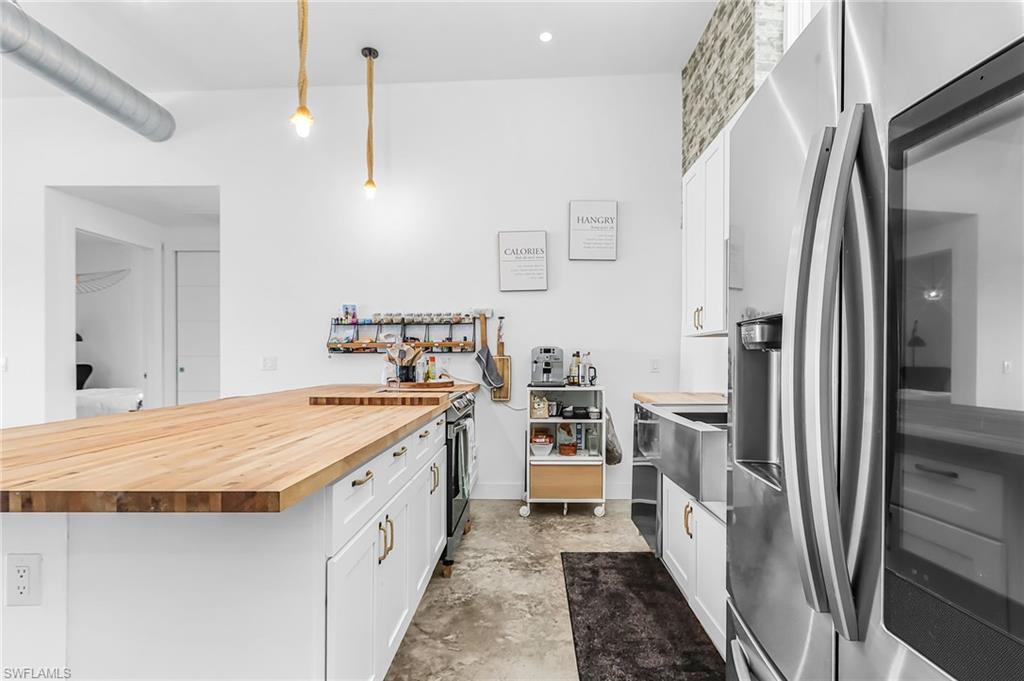 Kitchen with white cabinets, stainless steel appliances, wood counters, unfinished concrete flooring, and pendant lighting