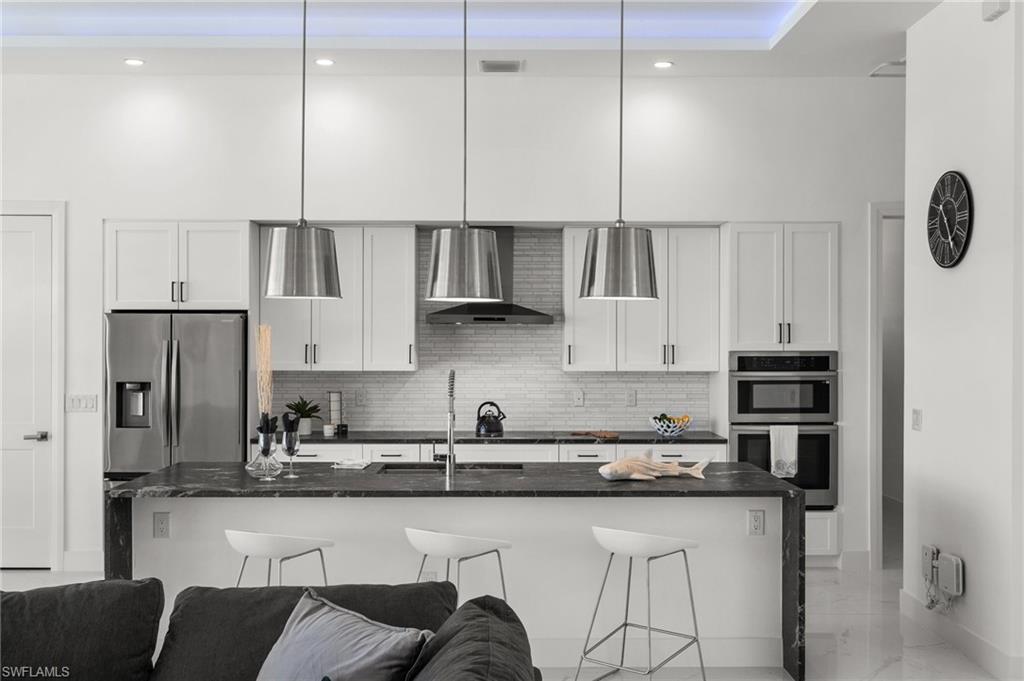 Kitchen featuring white cabinets, stainless steel appliances, dark stone countertops, a breakfast bar area, and decorative light fixtures