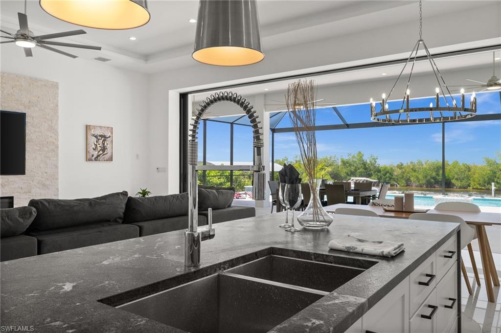 Kitchen featuring ceiling fan, open floor plan, hanging lights, and dark stone countertops