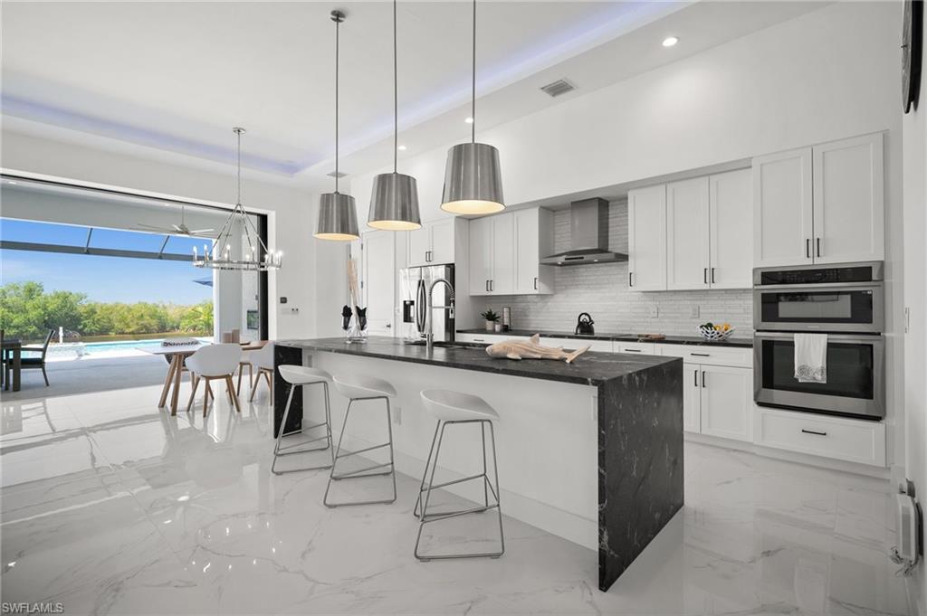 Kitchen with suspended lighting, an island with sink, a kitchen bar, stainless steel appliances, and white cabinetry