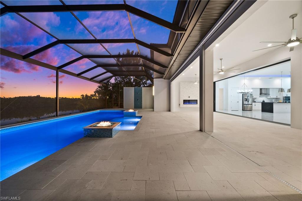 Outdoor pool featuring a sunroom, glass enclosure, an outdoor fire pit, a patio, and area for grilling