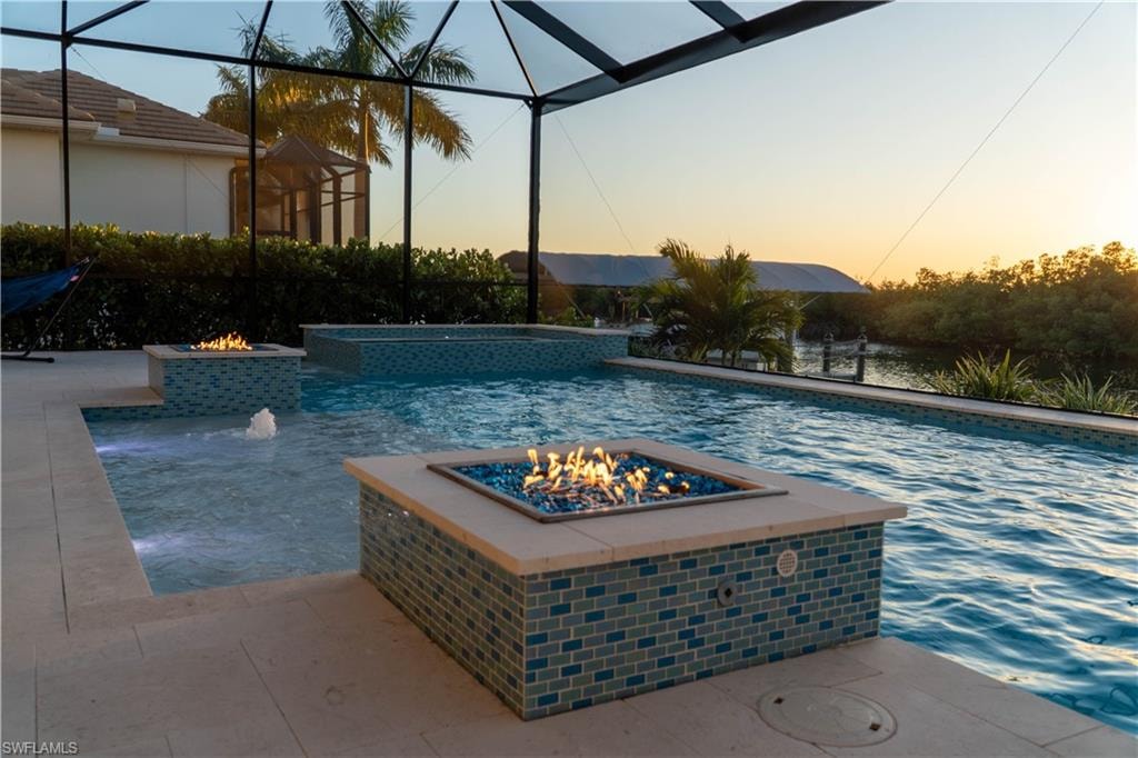 Pool at dusk featuring an outdoor fire pit, glass enclosure, a patio, and a pool with connected hot tub