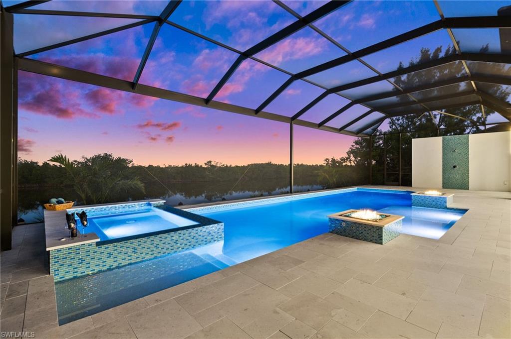 Pool at dusk featuring a pool with connected hot tub, glass enclosure, a patio area, and a sunroom