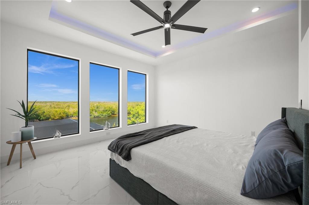 Bedroom featuring a raised ceiling, marble finish flooring, a ceiling fan, recessed lighting, and a water view
