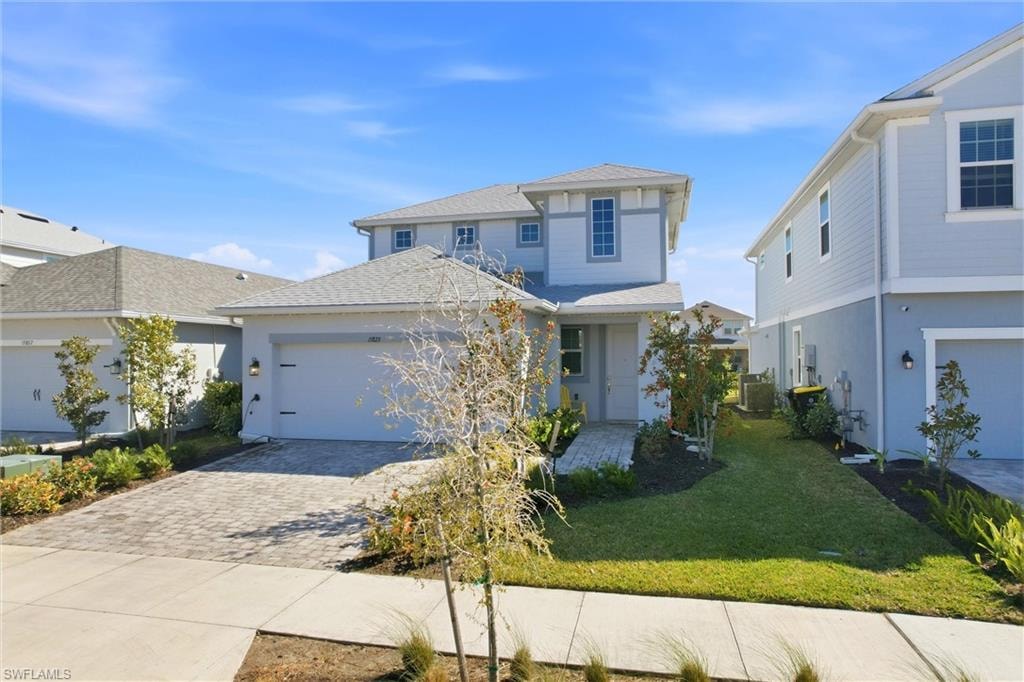 View of front of home featuring a front lawn, decorative driveway, a garage, and a shingled roof