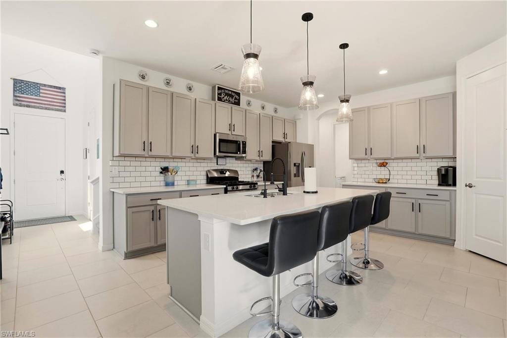 Kitchen with gray cabinetry, a kitchen bar, decorative light fixtures, a center island with sink, and stainless steel appliances