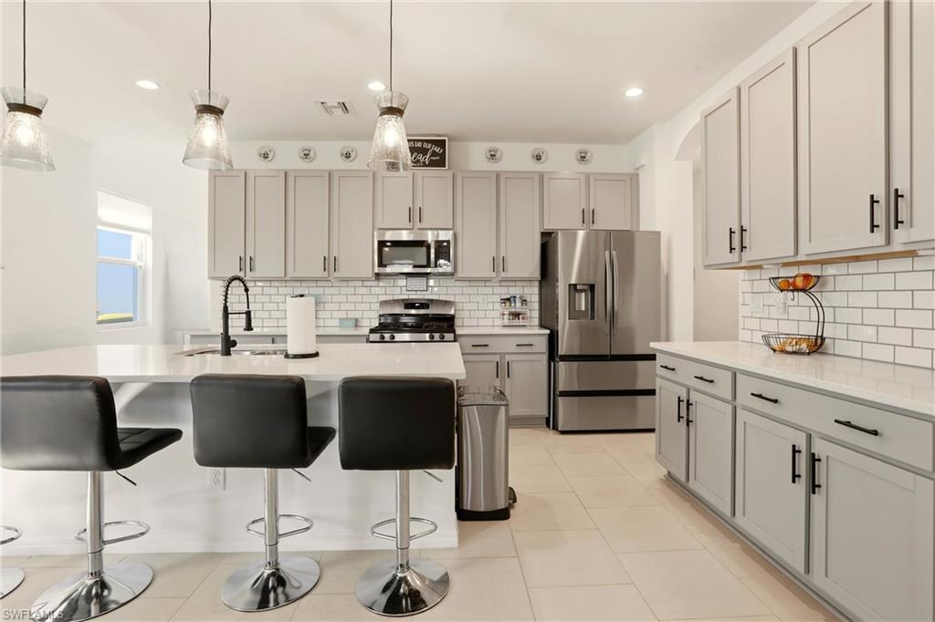Kitchen with stainless steel appliances, a kitchen bar, hanging light fixtures, light stone counters, and an island with sink