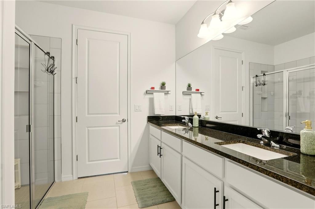 Bathroom featuring a shower stall, double vanity, and light tile patterned flooring