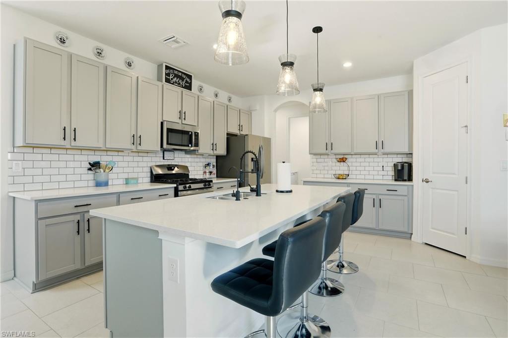 Kitchen with a breakfast bar, arched walkways, decorative light fixtures, gray cabinets, and stainless steel appliances