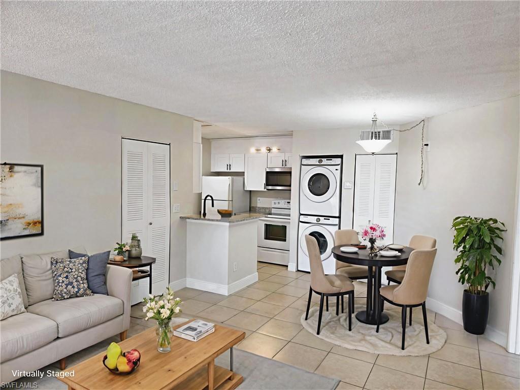 Living area with stacked washer / drying machine, light tile patterned flooring, and a textured ceiling
