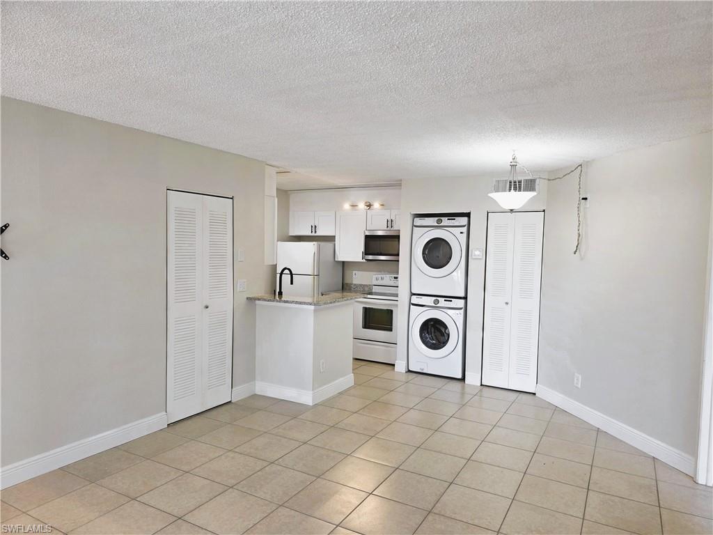 Kitchen with white appliances, white cabinetry, stacked washing machine and dryer, a peninsula, and a textured ceiling