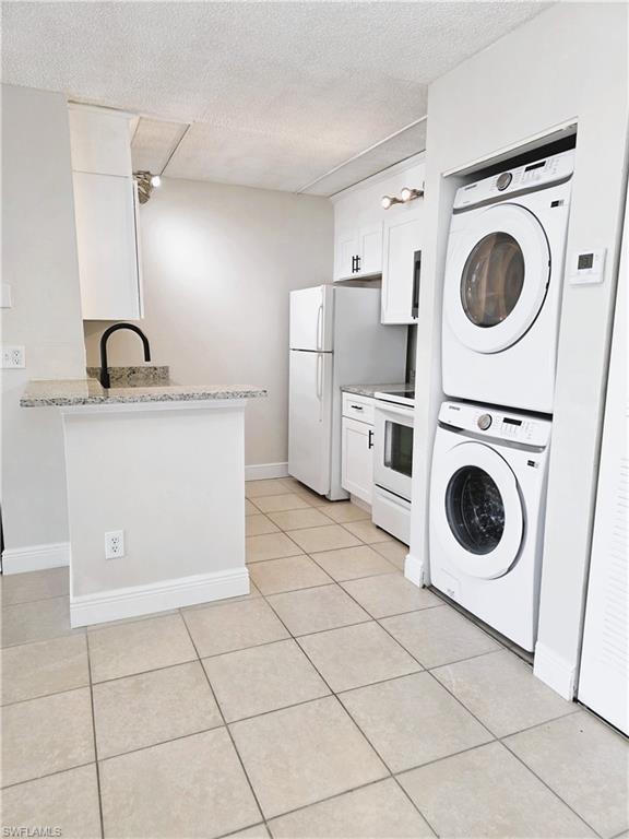 Kitchen with white cabinetry, stacked washer / dryer, a textured ceiling, white electric stove, and light tile patterned flooring