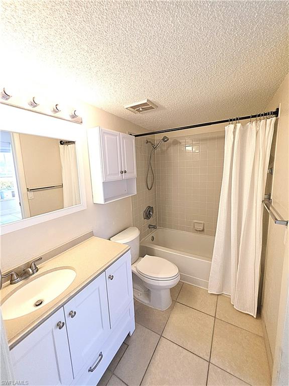 Full bath with vanity, shower / tub combo with curtain, a textured ceiling, and light tile patterned flooring