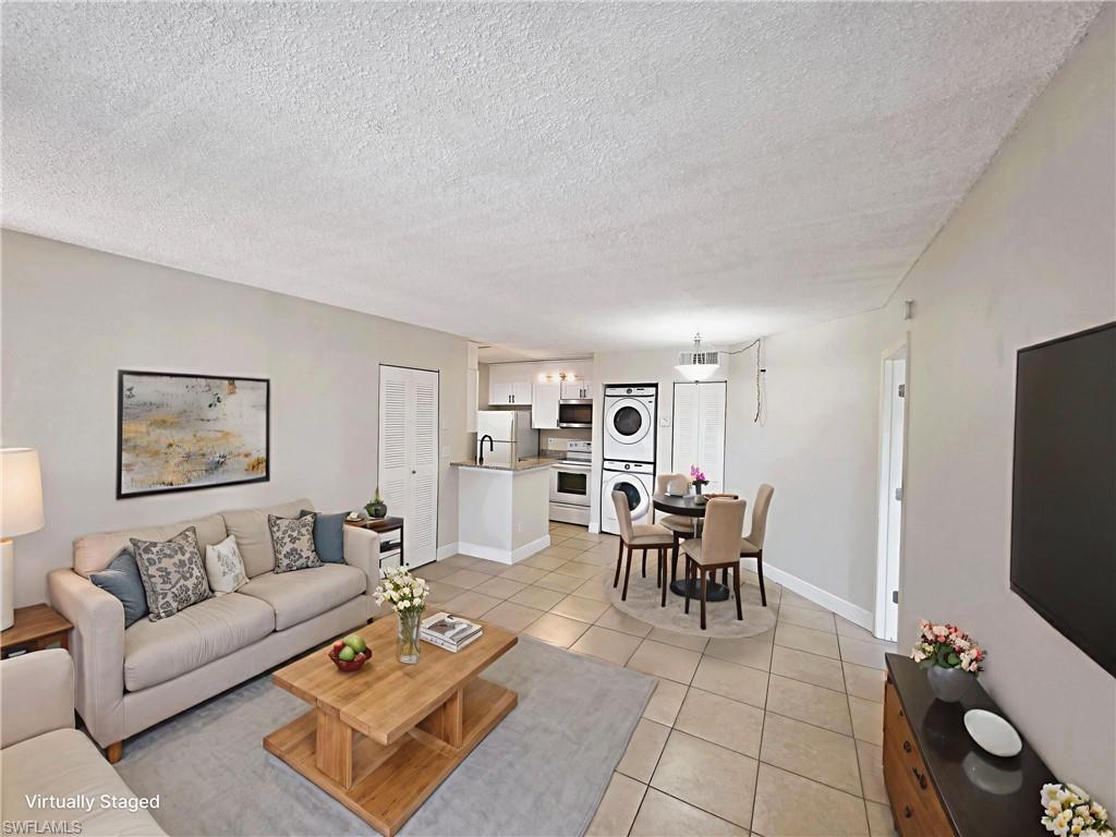 Living room with stacked washer / dryer, light tile patterned flooring, and a textured ceiling