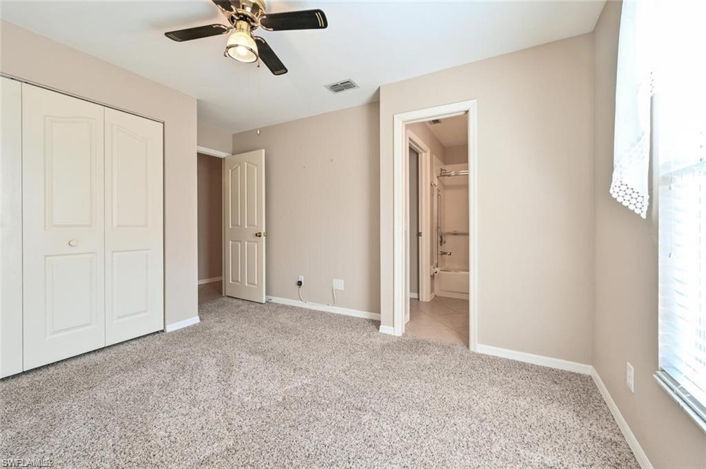 Unfurnished bedroom featuring ensuite bathroom, light colored carpet, a closet, and a ceiling fan