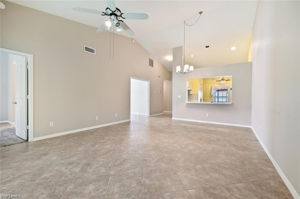 Unfurnished living room featuring a ceiling fan, vaulted ceiling, a chandelier, and light tile patterned flooring