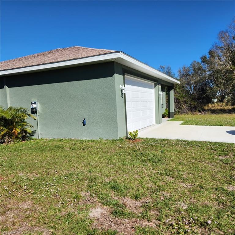View of side of home featuring stucco siding, a lawn, and concrete driveway