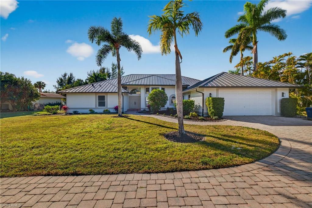 View of front facade featuring stucco siding, a front yard, curved driveway, and a metal roof