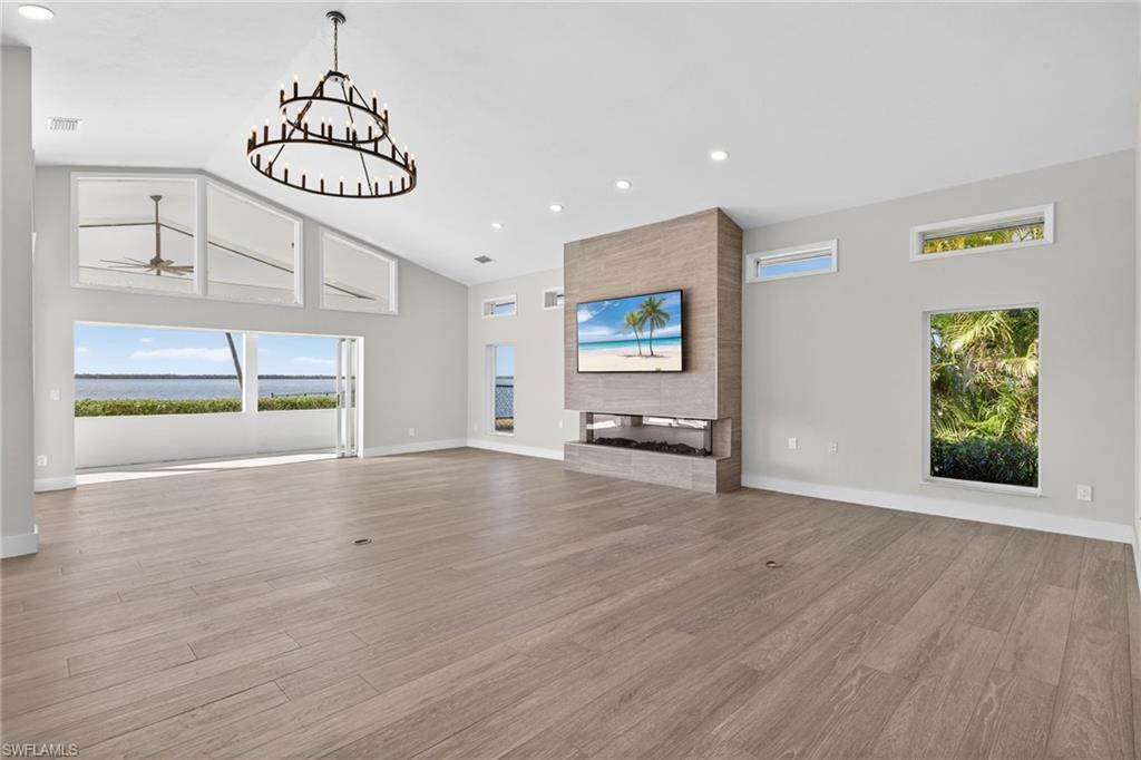 Unfurnished living room with a large fireplace, light wood-style flooring, vaulted ceiling, and hanging lights