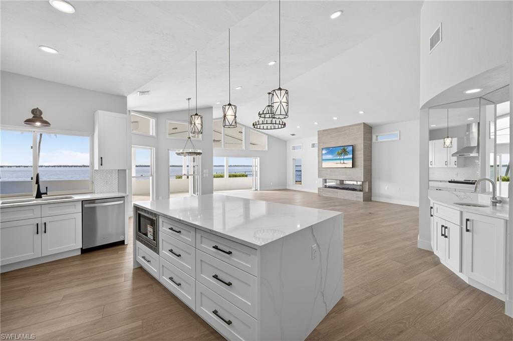 Kitchen with white cabinetry, light stone counters, pendant lighting, a kitchen island, and vaulted ceiling