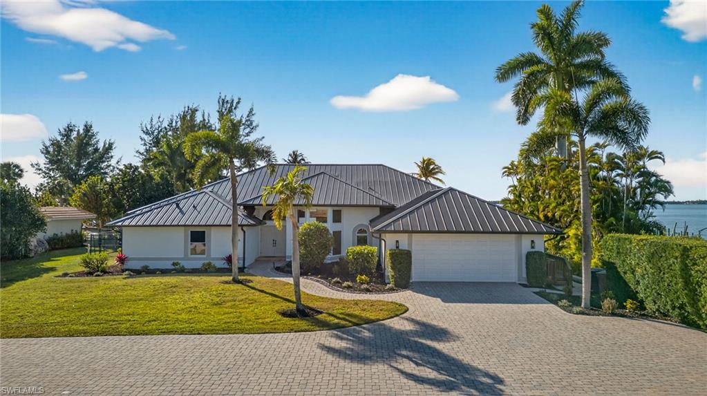 View of front of home with decorative driveway, a front yard, an attached garage, stucco siding, and a standing seam roof