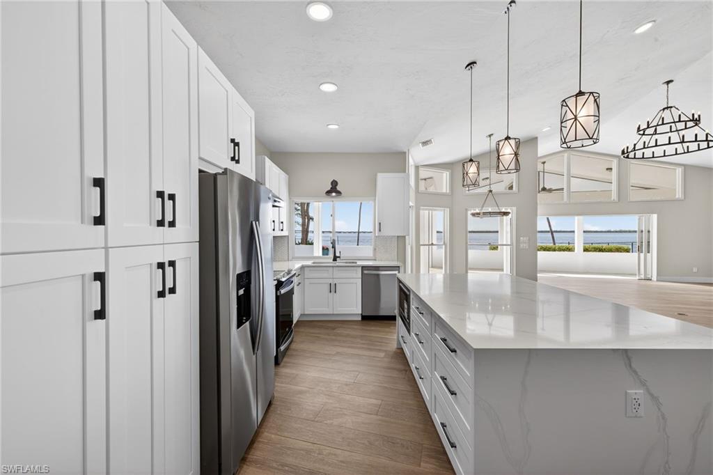 Kitchen featuring white cabinetry, stainless steel appliances, a large island, light wood-style flooring, and light stone counters