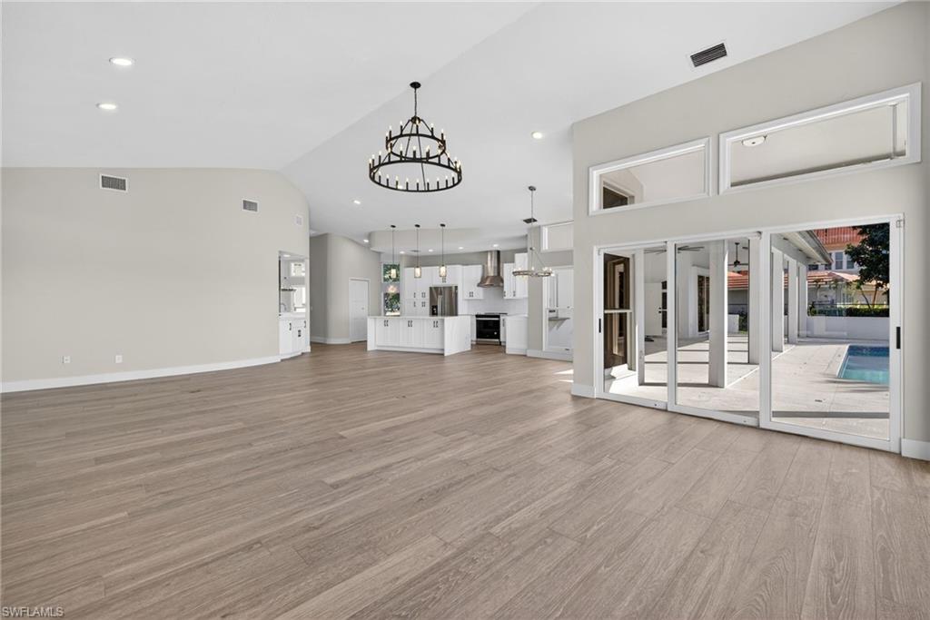 Unfurnished living room with suspended lighting, vaulted ceiling, and light wood-style flooring