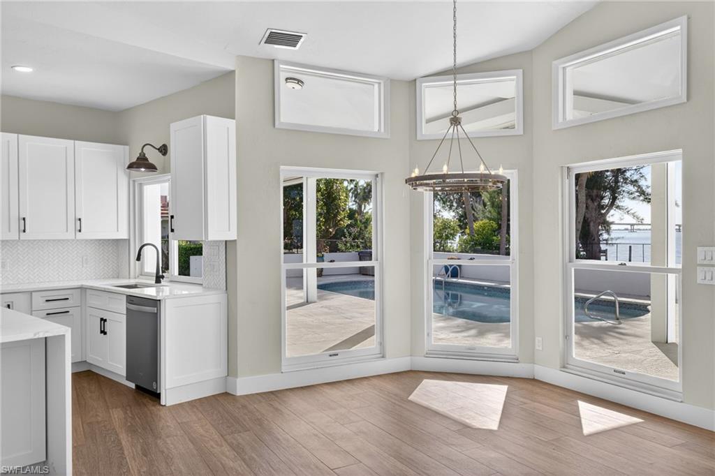 Kitchen with decorative backsplash, hanging lights, light stone counters, white cabinets, and light wood-style floors