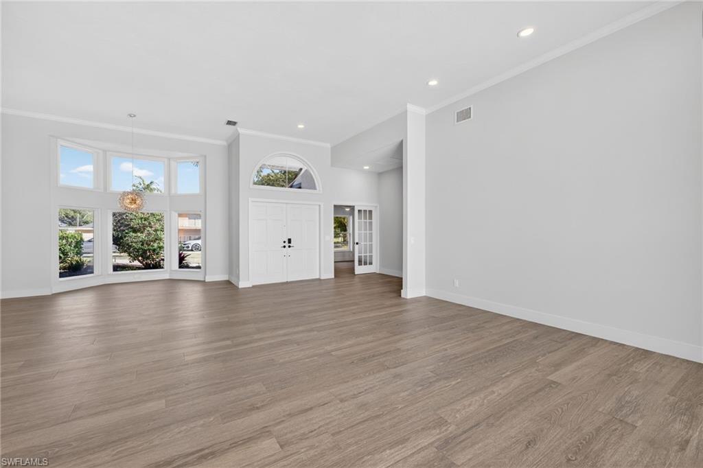 Unfurnished living room featuring healthy amount of natural light, a high ceiling, light wood-type flooring, ornamental molding, and recessed lighting