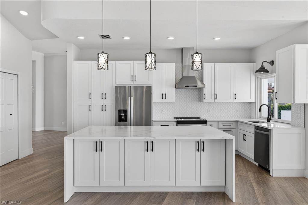 Kitchen with light stone countertops, stainless steel appliances, white cabinets, pendant lighting, and light wood-style floors