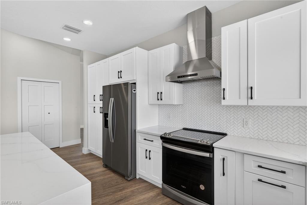 Kitchen with light stone counters, electric range oven, stainless steel fridge, white cabinets, and recessed lighting