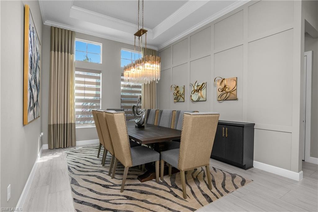 Dining room featuring suspended lighting, a decorative wall, crown molding, and a tray ceiling