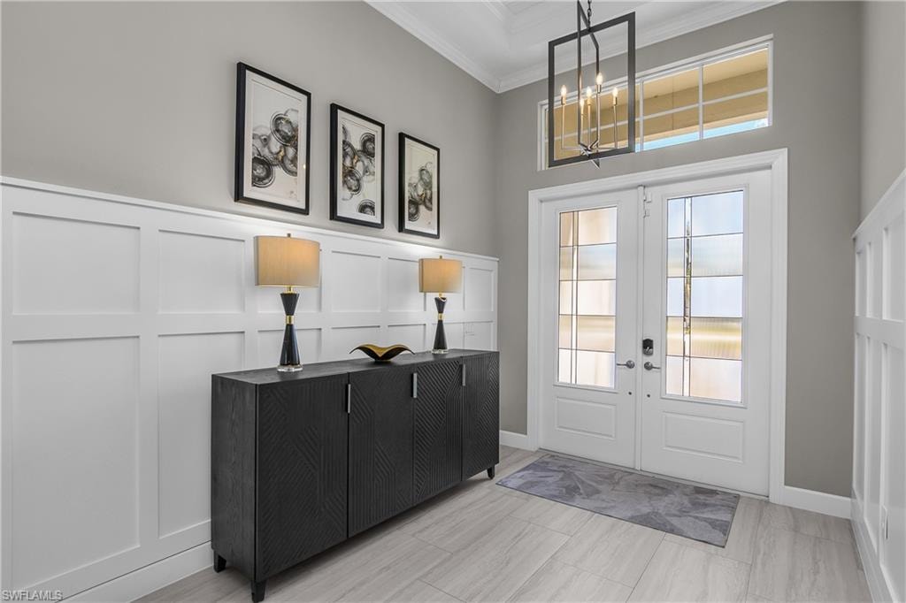 Entryway featuring french doors, a decorative wall, crown molding, and suspended lighting