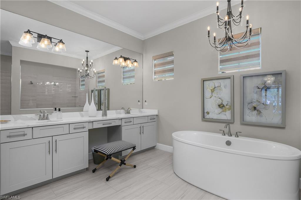 Bathroom with a chandelier, double vanity, a soaking tub, ornamental molding, and tiled shower