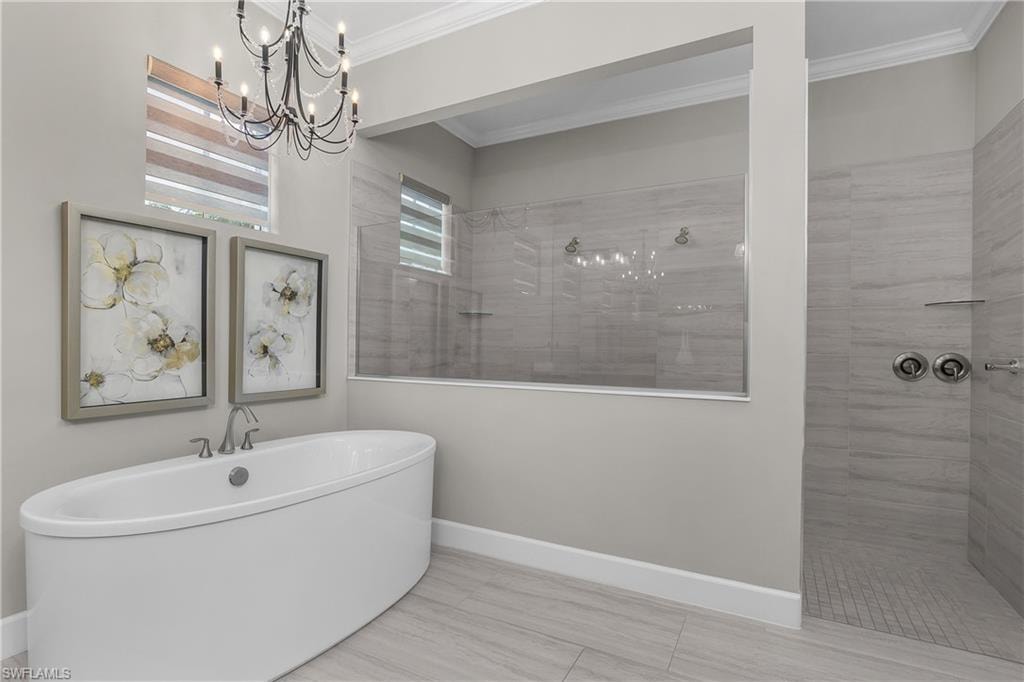 Full bath featuring walk in shower, crown molding, a chandelier, and a soaking tub