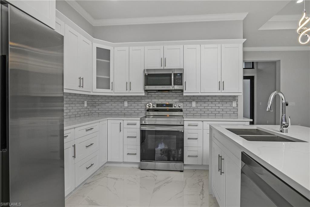 Kitchen featuring stainless steel appliances, ornamental molding, light stone countertops, and white cabinets
