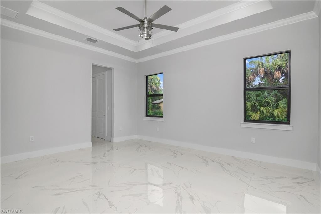 Empty room with ornamental molding, a ceiling fan, light marble finish flooring, and a tray ceiling