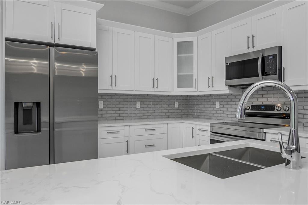 Kitchen featuring stainless steel appliances, white cabinets, light stone counters, glass fronted cabinets, and decorative backsplash