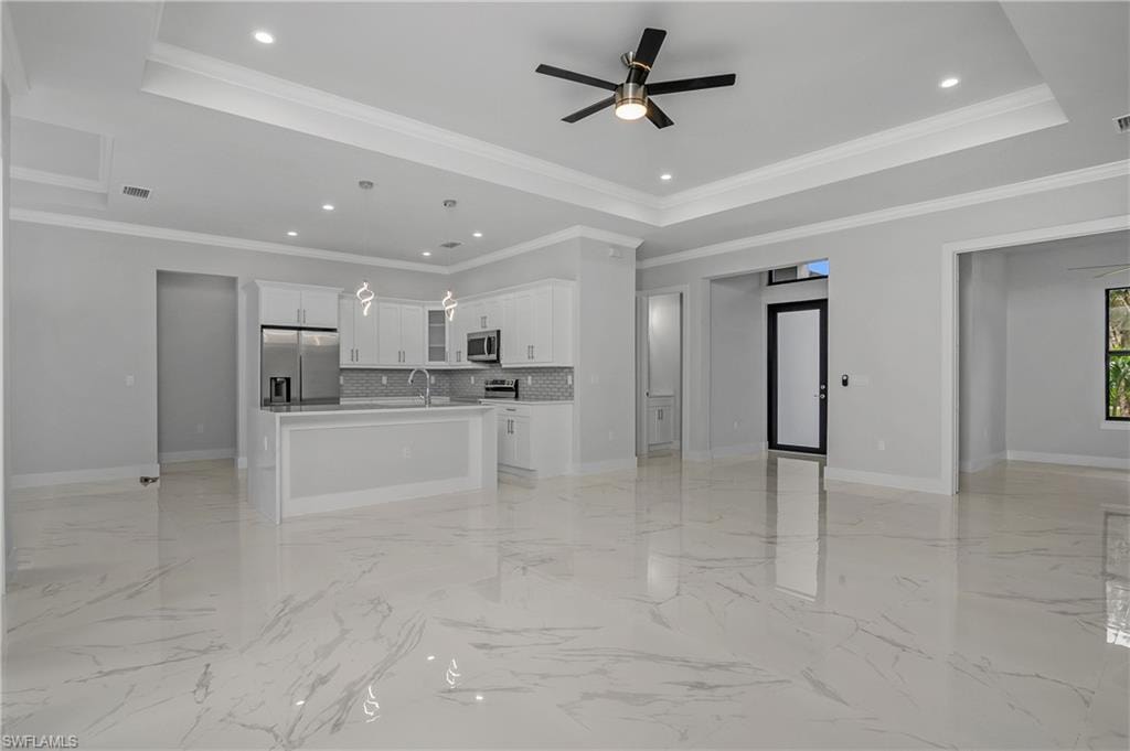 Unfurnished living room with a ceiling fan, ornamental molding, recessed lighting, and a tray ceiling