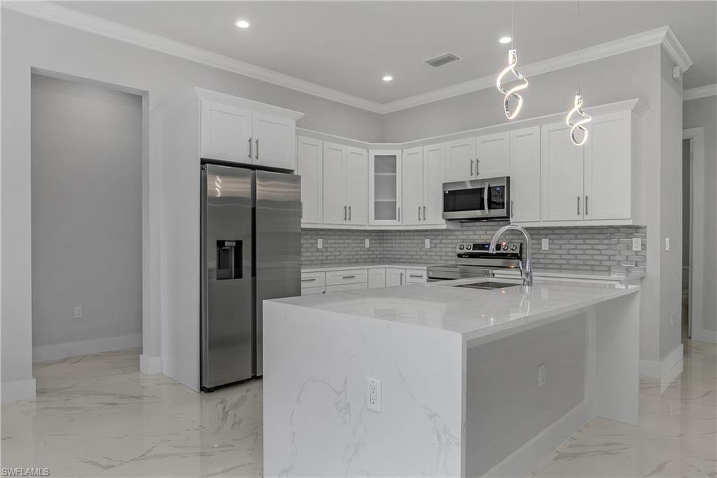 Kitchen featuring white cabinets, stainless steel appliances, ornamental molding, light stone counters, and hanging light fixtures