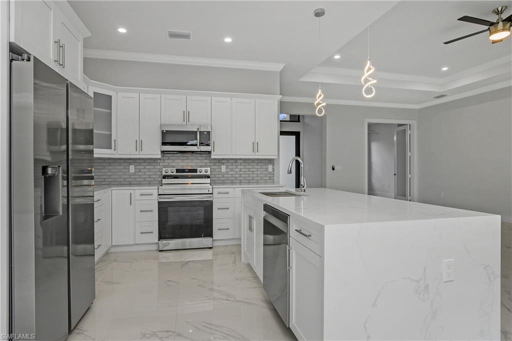 Kitchen with stainless steel appliances, crown molding, white cabinets, light marble finish floors, and a tray ceiling