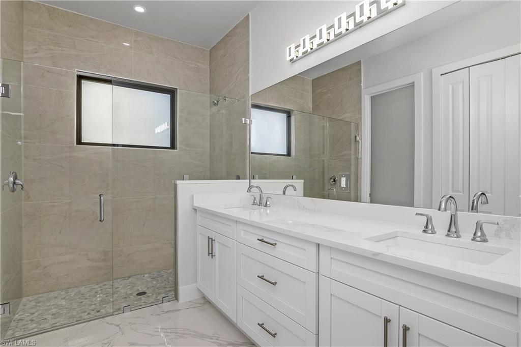 Full bath with a shower stall, double vanity, light marble finish floors, and a closet