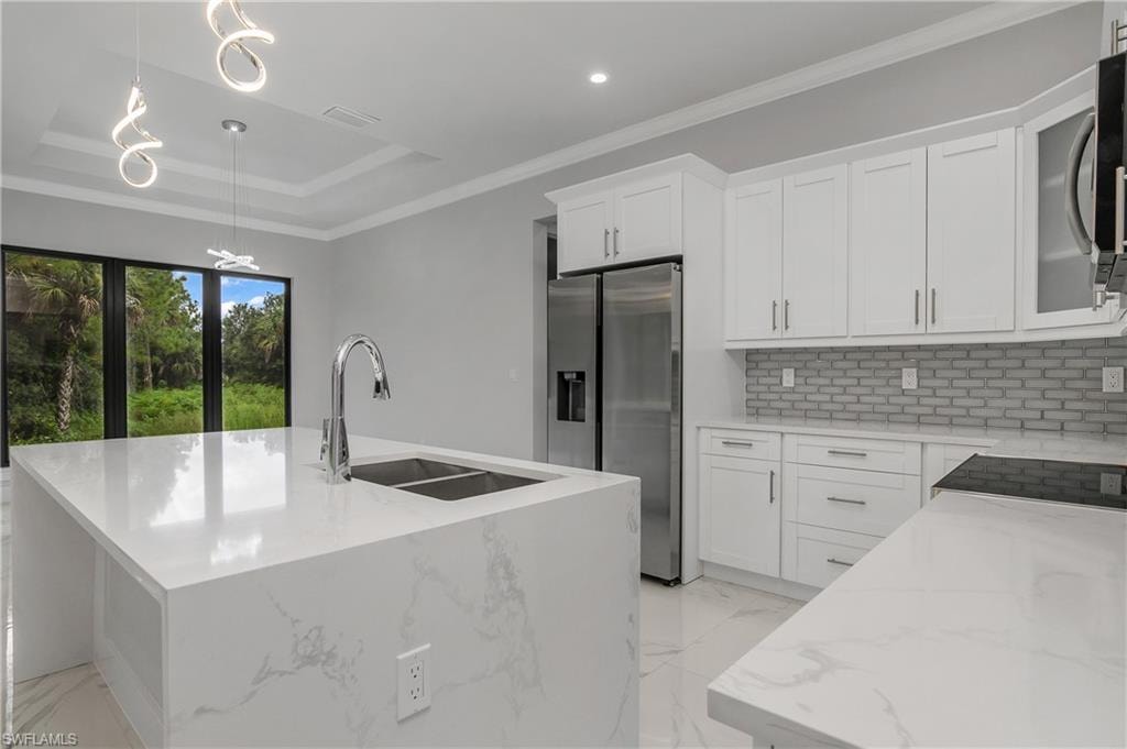 Kitchen with light stone countertops, decorative light fixtures, stainless steel appliances, crown molding, and an island with sink