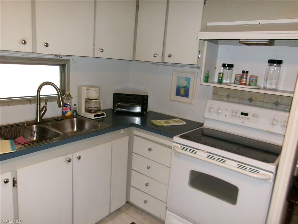 Kitchen featuring white electric stove, white cabinets, open shelves, and light tile patterned flooring