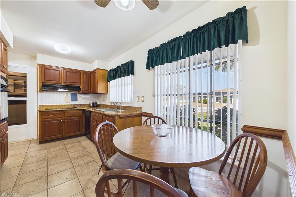 Kitchen with light tile patterned floors, ceiling fan, backsplash, wood finish cabinets, and dark stone counters