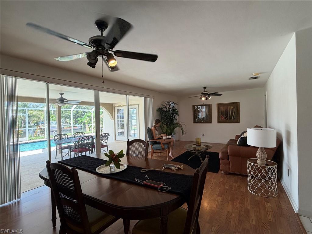 Open-concept interior featuring wood-finish flooring, ceiling fans, and sliding glass doors opening to a screened patio with a swimming pool